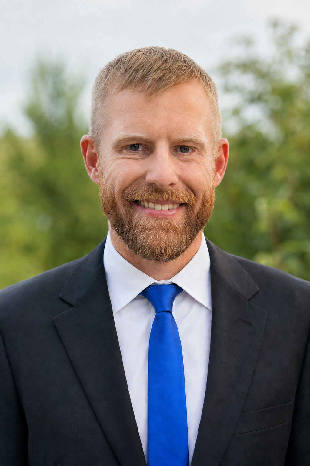 Bryan Burke smiling in a dark suit and blue tie outdoors
